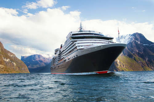 Das Kreuzfahrtschiff Queen Victoria fährt auf tiefblauem Wasser durch ein enges Tal zwischen steilen, schneebedeckten Bergen unter blauem Himmel.